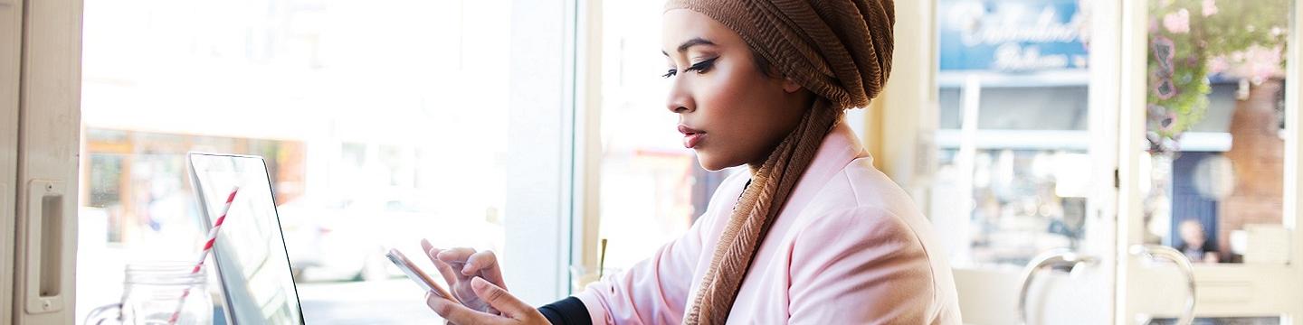 Woman scrolling in her phone in front of a computer at a café