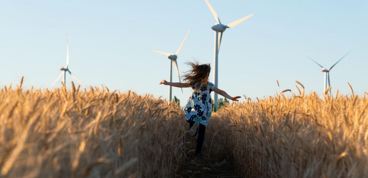 Girl in floral dress running through field towards wind turbines