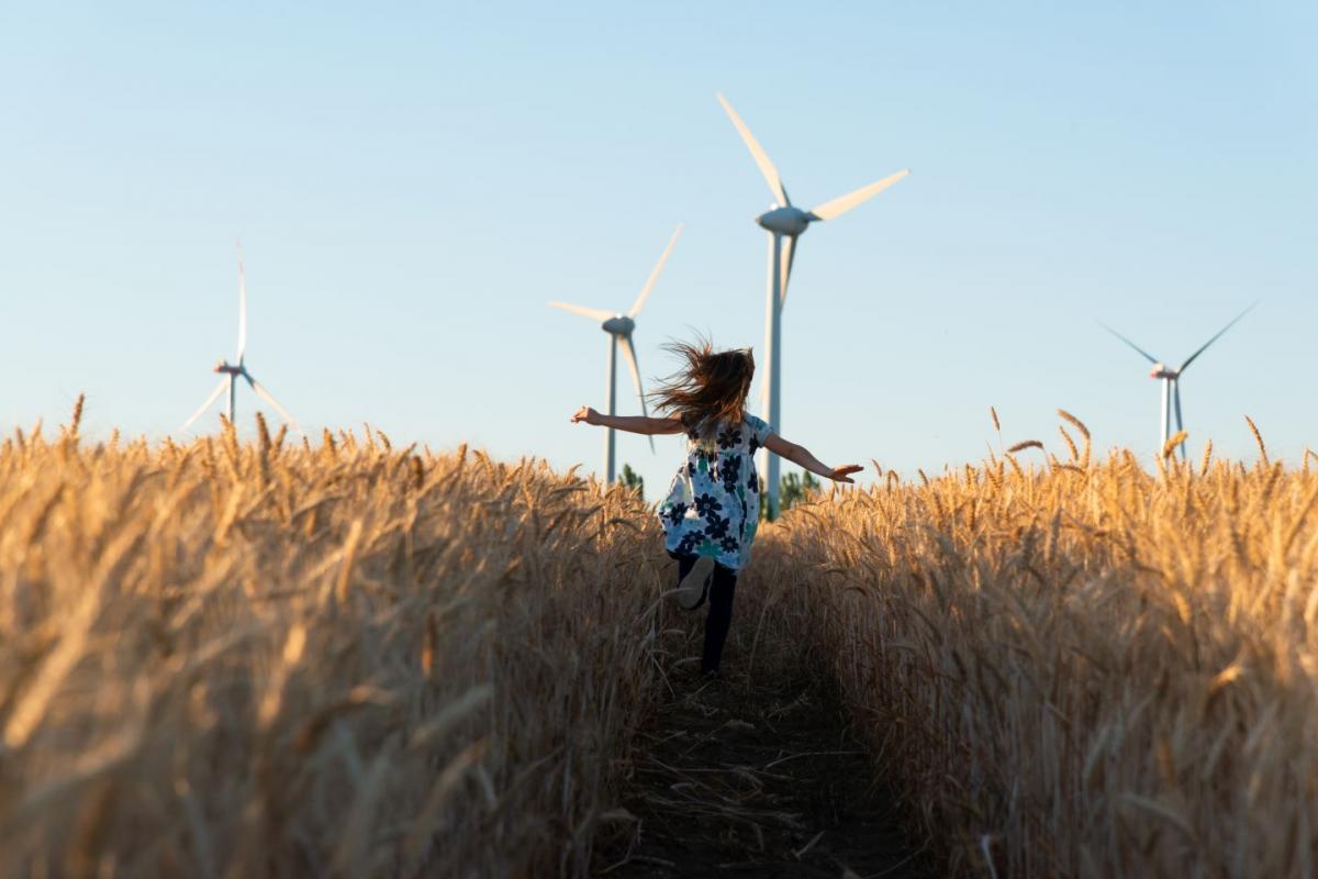 Girl in floral dress running through field towards wind turbines