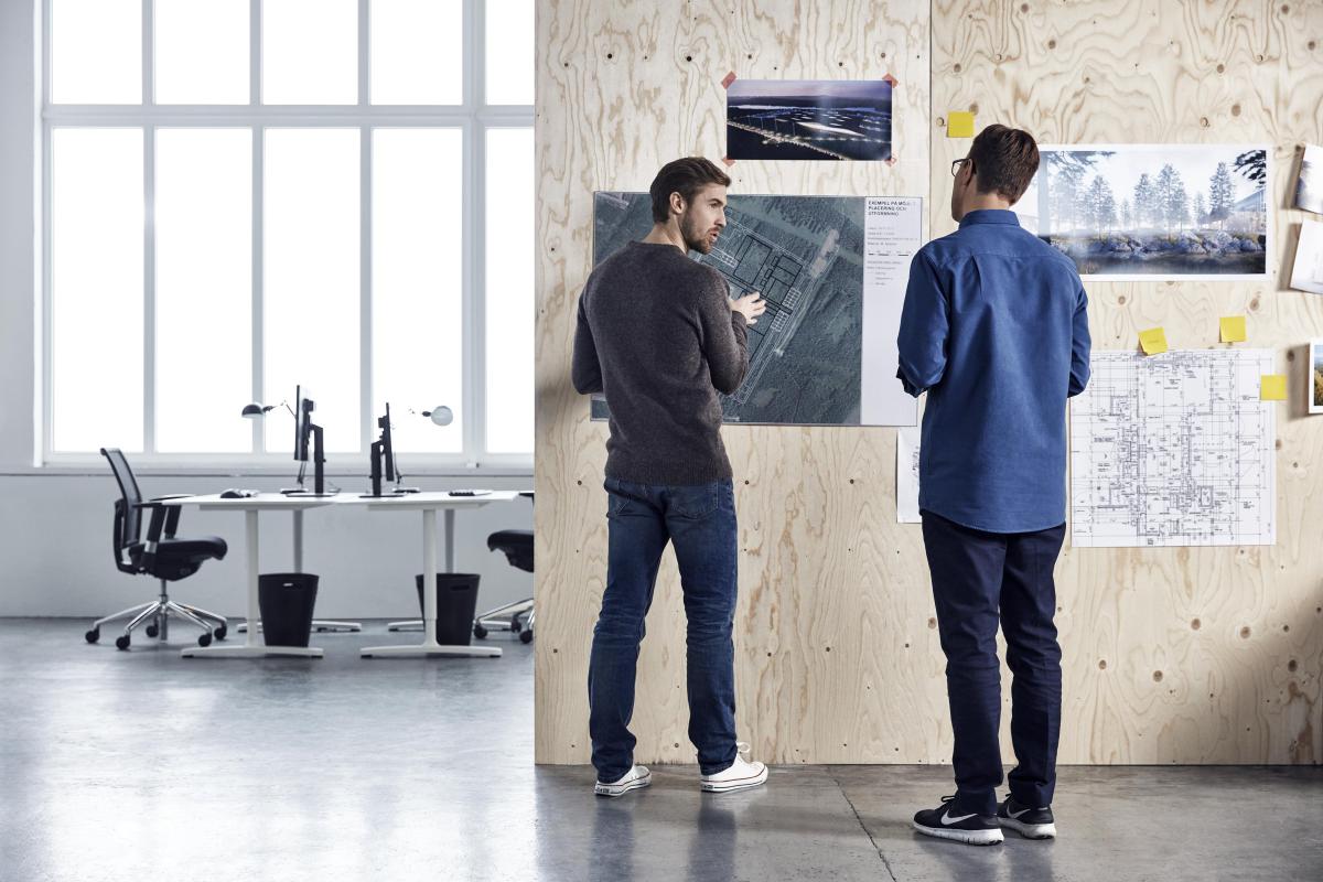 Two men standing in a office discussing technical drawings 