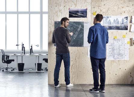 Two men standing in a office discussing technical drawings 