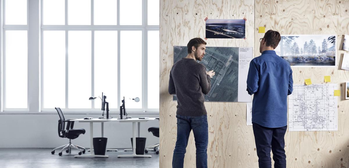 Two men standing in a office discussing technical drawings 