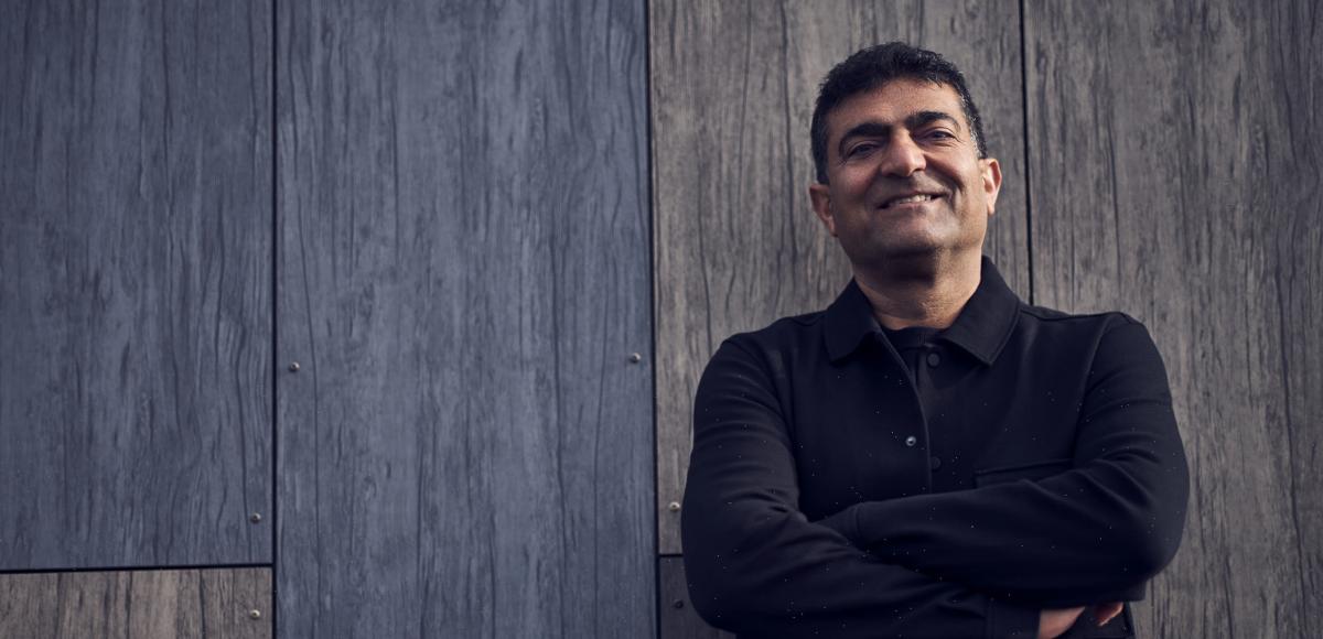 a man in a black jacket stands with his arms crossed and smiles at the camera