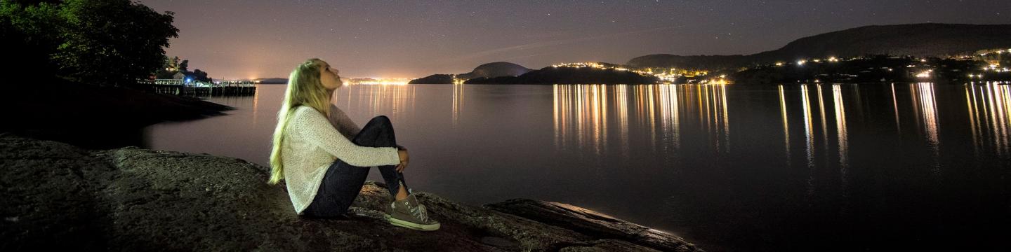 A woman sitting on a rock looking up on a sky full of stars