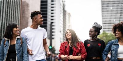 five people are walking down a street in a city and happily talking to each other