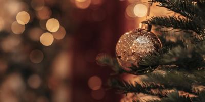 Gold bauble hanging from a fir tree with fairy lights in background