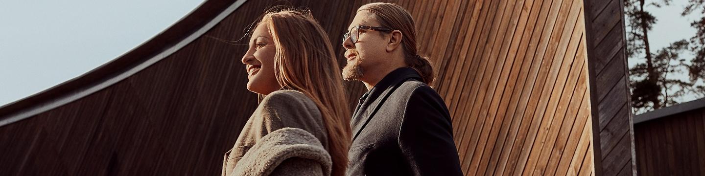 Man with long hair and glasses and a women with a grey coat are looking away to the left