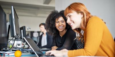 two women in front of a laptop, laughing