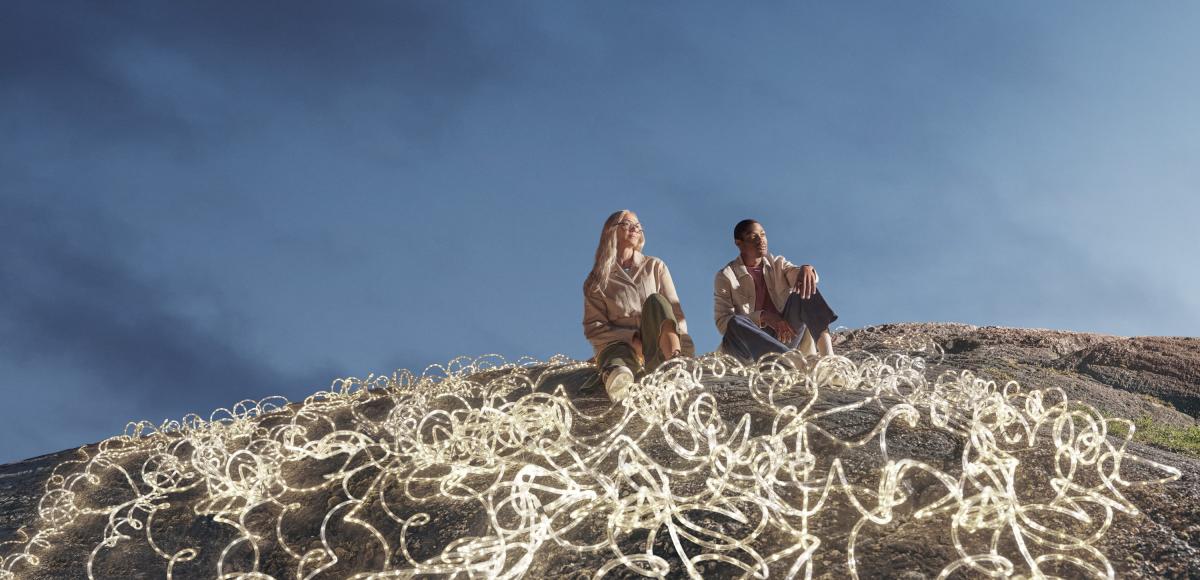 Expansive dark blue-sky backdrop, with a man and woman in the foreground surrounded by white LED rope lights.