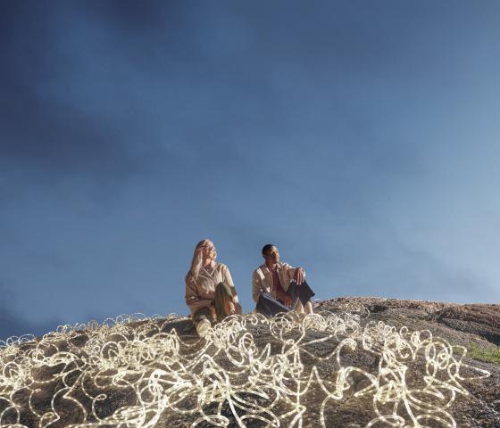 Expansive dark blue-sky backdrop, with a man and woman in the foreground surrounded by white LED rope lights.