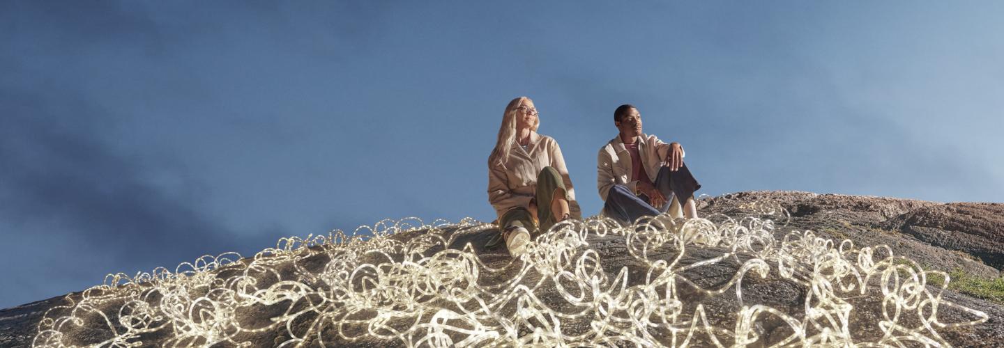 Expansive dark blue-sky backdrop, with a man and woman in the foreground surrounded by white LED rope lights.