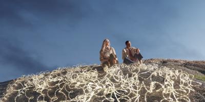 Expansive dark blue-sky backdrop, with a man and woman in the foreground surrounded by white LED rope lights.