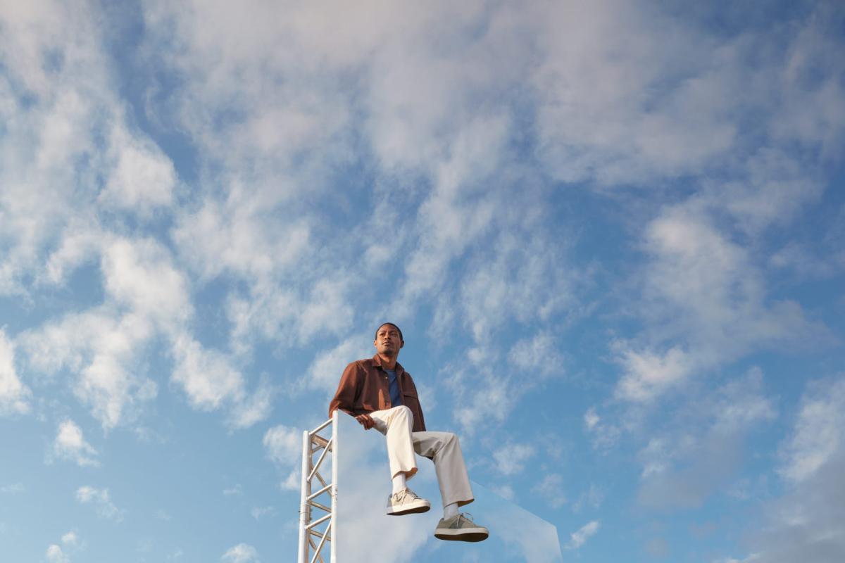 Expansive light blue-sky backdrop, with a man in the foreground sitting on top of large mirror