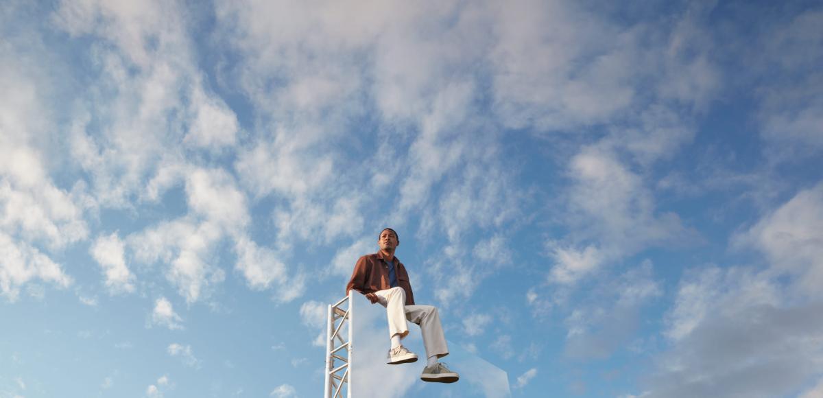 Expansive light blue-sky backdrop, with a man in the foreground sitting on top of large mirror