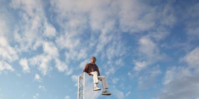 Expansive light blue-sky backdrop, with a man in the foreground sitting on top of large mirror
