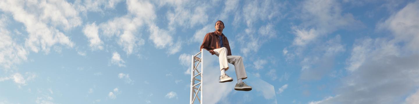 Expansive light blue-sky backdrop, with a man in the foreground sitting on top of large mirror