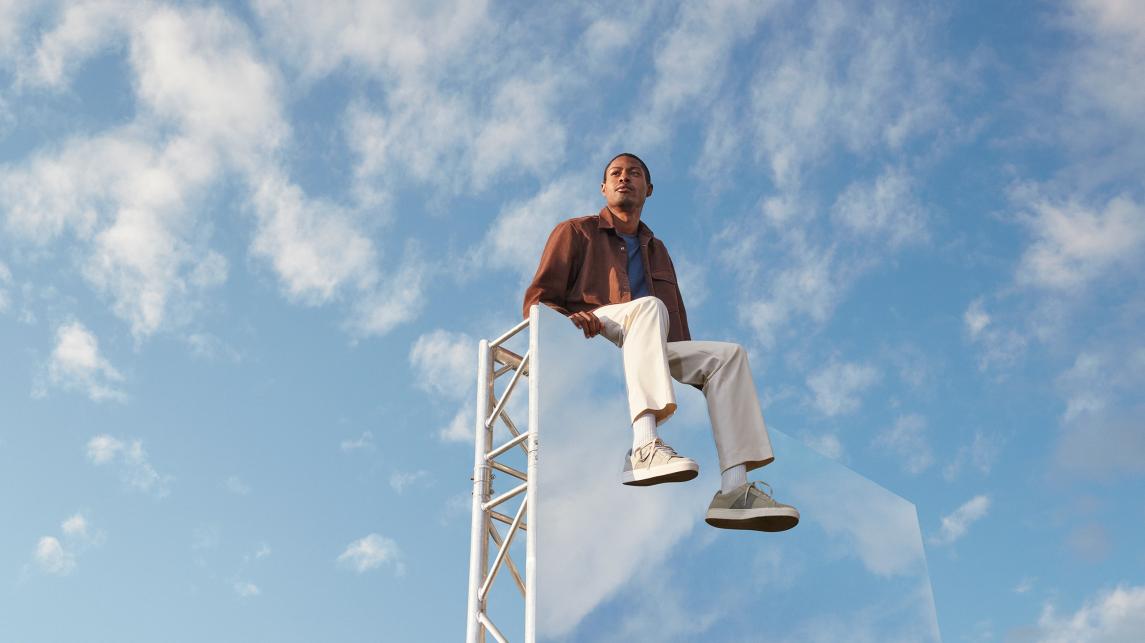 Expansive light blue-sky backdrop, with a man in the foreground sitting on top of large mirror
