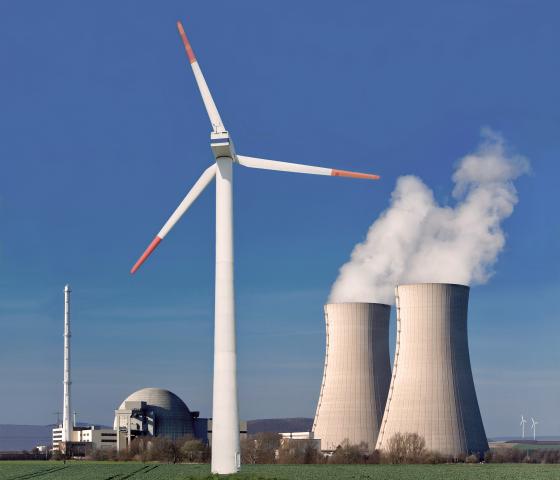 Wind turbine in a green field in front of a nuclear power plant under a blue sky