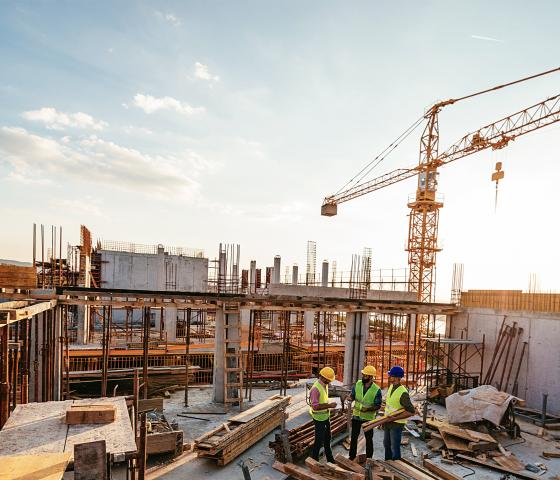 Two construction workers on a construction site, wearing vests and security helmets