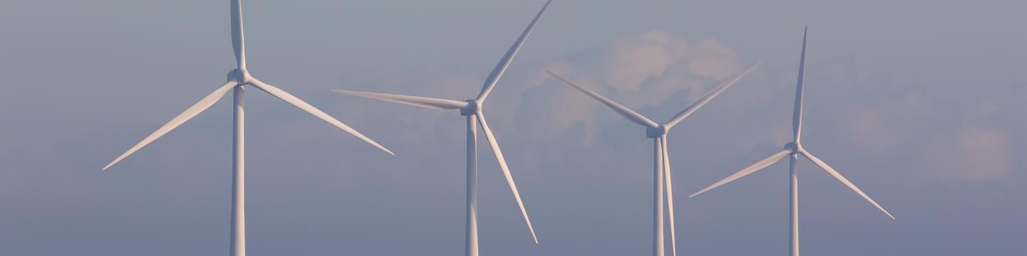 Offshore wind turbines. Green energy. Row of four environmentally friendly wind powered turbines on the sea horizon off the coast of Great Yarmouth UK.