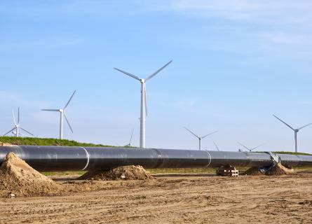 Pipeline construction site on a sunny day, windmill farm in background