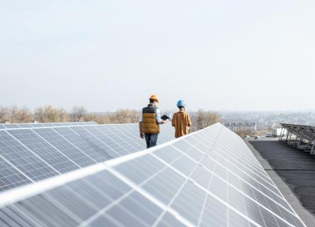 View on the rooftop solar power plant with two engineers walking and examining photovoltaic panels. Concept of alternative energy and its service