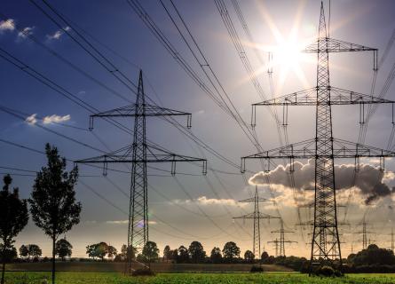 Transmission towers and lines standing on a green field under the sun