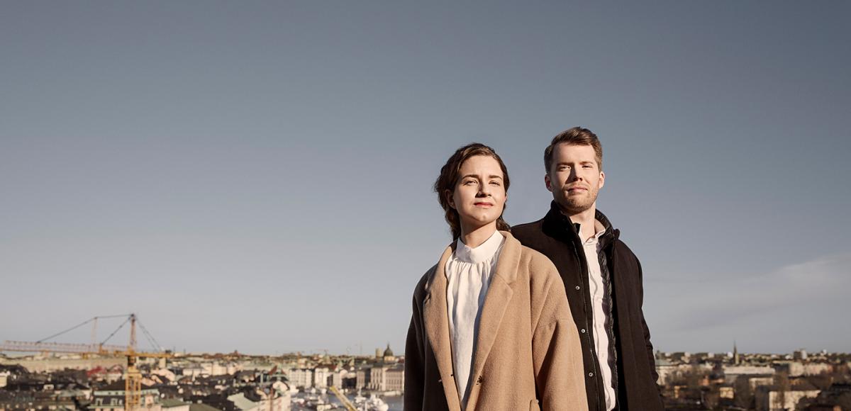A man and a woman standing on a rooftop looking out over the city