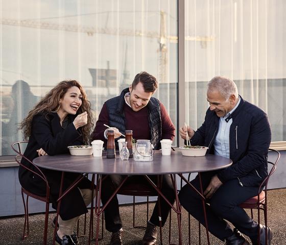 A woman and two men eating lunch outside.